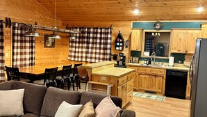 A cozy cabin interior with a wooden ceiling, a dining area, a kitchen with wooden cabinets, and a gray sofa with cushions. - Greer Mountain Cabin: Scenic Deck, Rustic Charm & Stress-Free Parking (Greer)