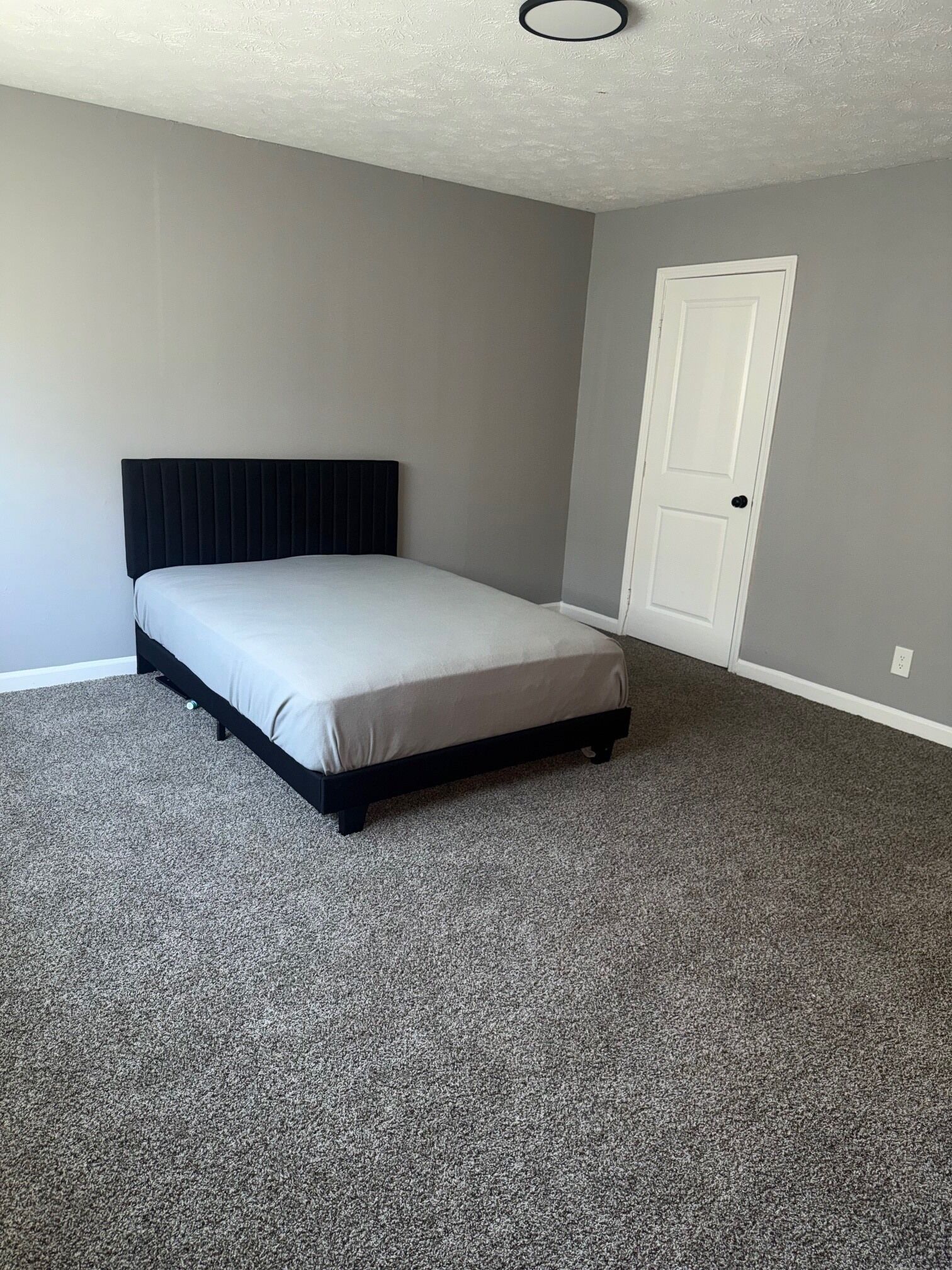 A bedroom with a single bed, a door, and a textured ceiling.