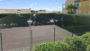 Ein Tennisplatz mit Zaun, einer Laterne und einem Gebäude mit Ziegeldach im Hintergrund.