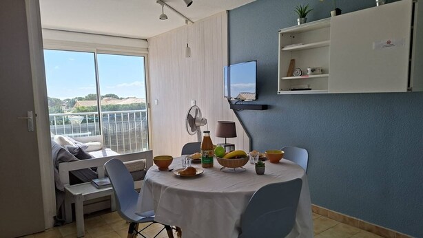 Ein Essbereich mit Tisch für zwei Personen, einem Ventilator, einem Fernseher und einem Balkon mit Blick.