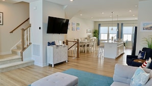 A modern living room with a staircase, a dining area, and a kitchen in the background. - Bayside Break | Rooftop Deck + Resort Pools & Gym (Berlin)
