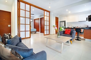 A modern living room with a sofa, coffee table, and a kitchen area in the background. - Cozy 1BR Condo in TAO Akumal w/ Terrace (Akumal)
