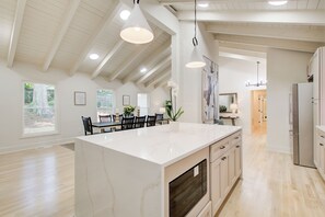 Une cuisine spacieuse dotée d’un grand îlot central, de planchers en bois et de luminaires suspendus.