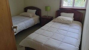 Een kamer met twee bedden, een nachtkastje met een lamp en een raam met zonwering.
