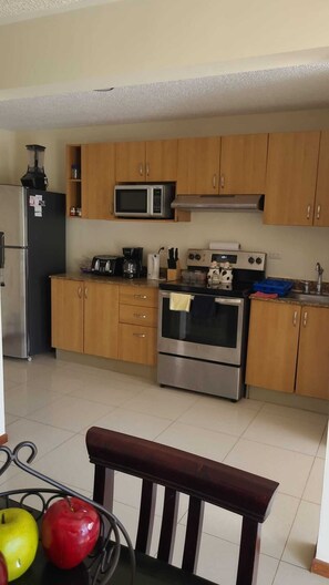 A kitchen with wooden cabinets, a microwave, a refrigerator, a stove, and a sink. - Beautiful Costa Linda beach condo, 2 BR/ 2 BA, Pool view (Jacó)
