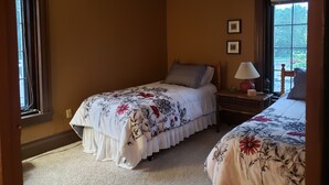 A bedroom with two beds, a ceiling fan, a window with a view, and a nightstand with a lamp.