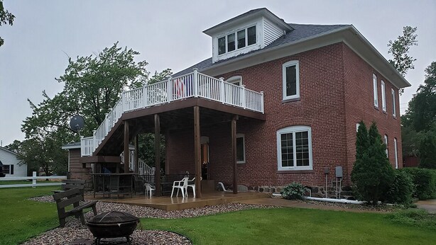 A two-story brick house with a covered patio, outdoor seating, and a fire pit.