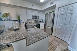 A modern kitchen with granite countertops, stainless steel appliances, and white cabinetry. - Sunset Serenity 1302-Gulf Views-Sleeps 6 (Panama City)