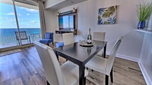 A modern dining area with a large table, chairs, a TV, and a view of the ocean.