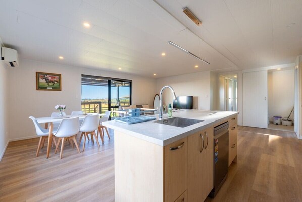 A modern kitchen with a large island, a dining area with white chairs, and a view through the window.