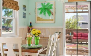 A dining area with a table set for two, a pitcher of green drinks, and a vase of yellow flowers. - Beachside Cottage with Private Hot Tub & Near Beach (Port Aransas)