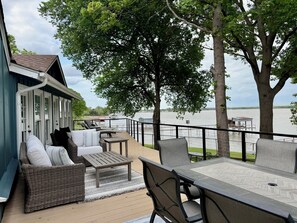 Eine Terrasse mit Gartenmöbeln, Blick auf ein Gewässer und ein Gebäude mit blauer Fassade.