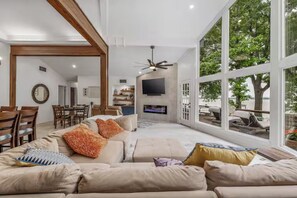 Un salon spacieux avec un grand canapé, un téléviseur fixé au mur et un coin repas doté de meubles en bois.