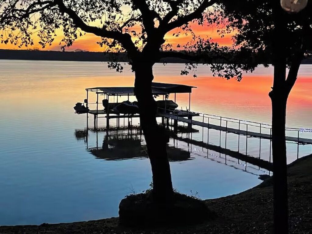 Un lago tranquilo al atardecer con un muelle y una estructura cubierta.