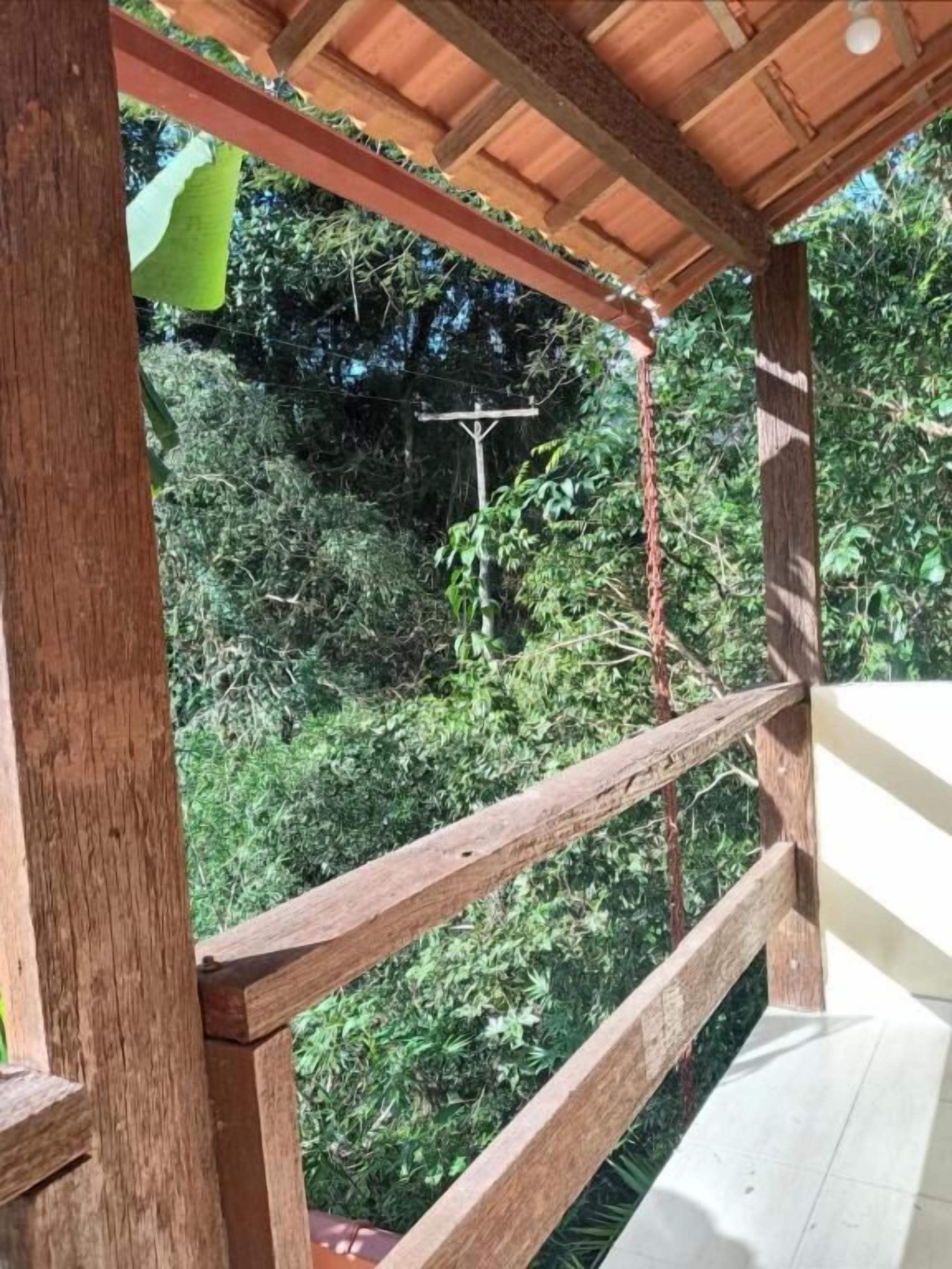 A wooden balcony with a view of dense greenery and a wooden structure in the background.