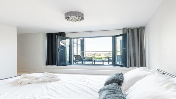 A hotel room with a large bed, a view of the outdoors, a chandelier, and a balcony with a chair. - Penthouse apartment in the centre of rayleigh - Pass the Keys (Rayleigh)