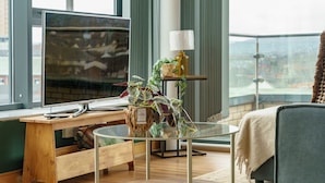 Une pièce moderne dotée d’une grande fenêtre, d’un bureau avec un ordinateur, d’une table en verre, d’un canapé et d’une plante.