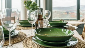 Une table à manger dressée avec des assiettes vertes, des verres transparents et un vase contenant des feuilles vertes.