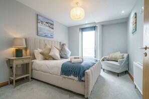 Un dormitorio con cama, mesita de noche, lámpara y ventana.