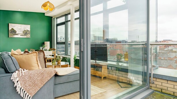 Un salon moderne avec un mur vert, un canapé gris et un coin repas comprenant une table et des chaises.