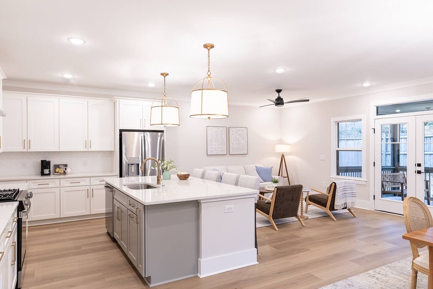 A modern kitchen with a central island, stainless steel appliances, pendant lighting, and a dining area with a sofa and chairs.
