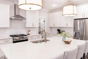 A modern kitchen with white cabinetry, stainless steel appliances, and a central island with a sink. - BR Speakeasy Near Duke + Theatre | Sleeps 12 (Durham)