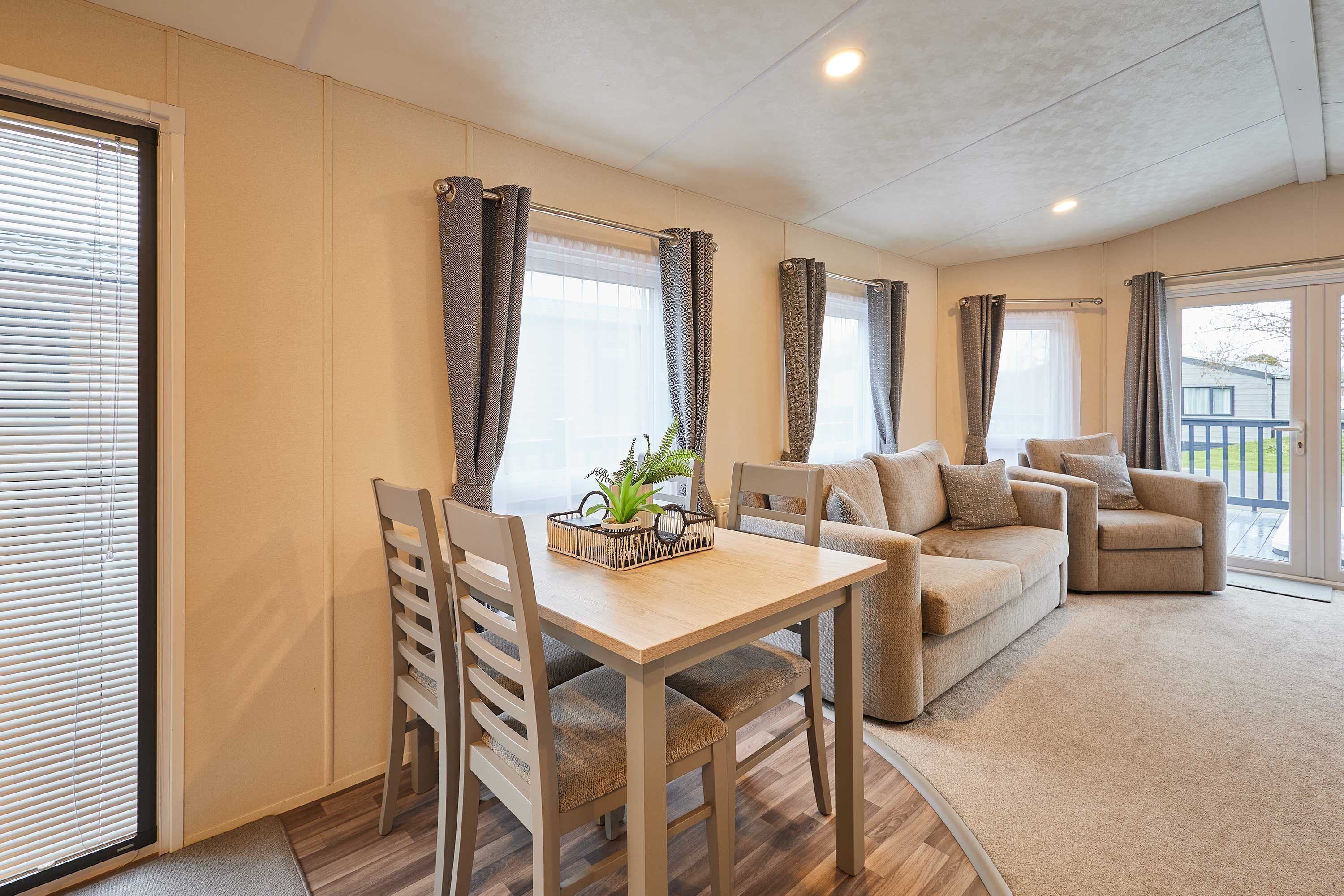 A living room with a sofa, a dining table, and chairs. There is a plant on the table.