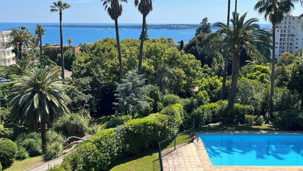 Una piscina circondata da vegetazione rigogliosa e palme, con vista sul mare e sugli edifici sullo sfondo.