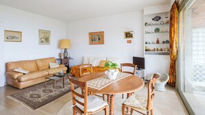 Un soggiorno con divano, tavolino, tavolo da pranzo, sedie, televisore e libreria con oggetti decorativi.