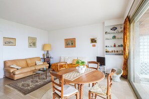 Ein Wohnzimmer mit einer Couch, einem Couchtisch, einem Esstisch, Stühlen, einem Fernseher und einem Bücherregal mit Dekoration.