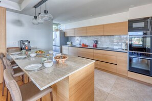 Une cuisine moderne dotée d’un îlot central, de meubles en bois, d’appareils électroménagers en acier inoxydable et de luminaires suspendus.