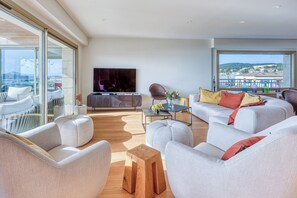 Un salon moderne doté d’un grand téléviseur, de sièges confortables, d’une table basse en bois et d’un balcon offrant une vue agréable.