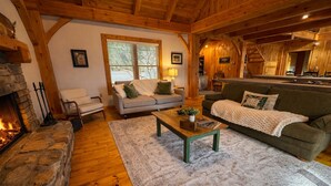 A cozy living room with a stone fireplace, wooden beams, a sofa, a coffee table, and a window with blinds. - Peaceful Resort Cabin in Sapphire Valley close to Cashiers & resort access (Sapphire)