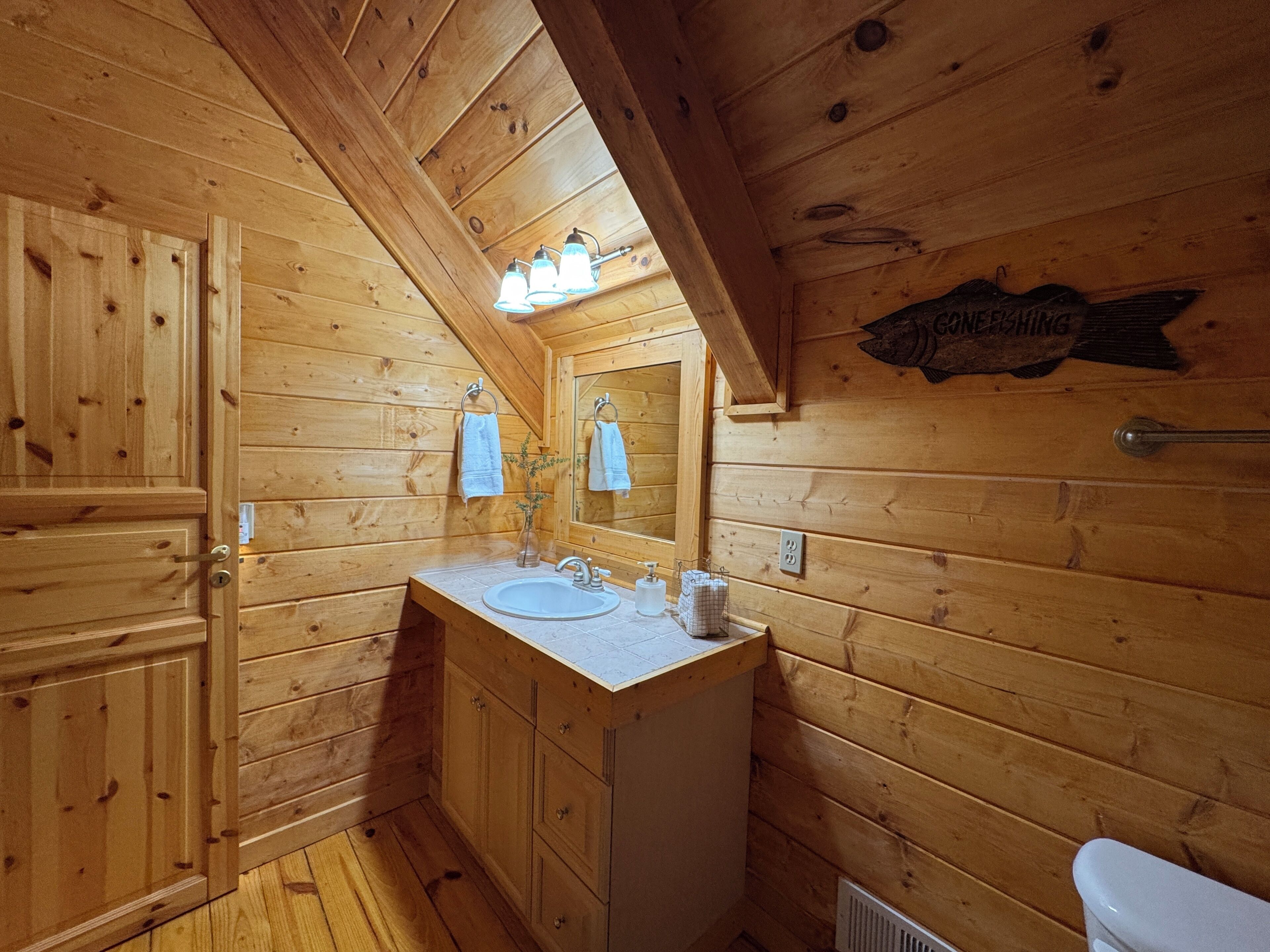 Baño de cabaña de madera con lavamanos, espejo, toallero y un cartel que dice 'GUNFISHING'.