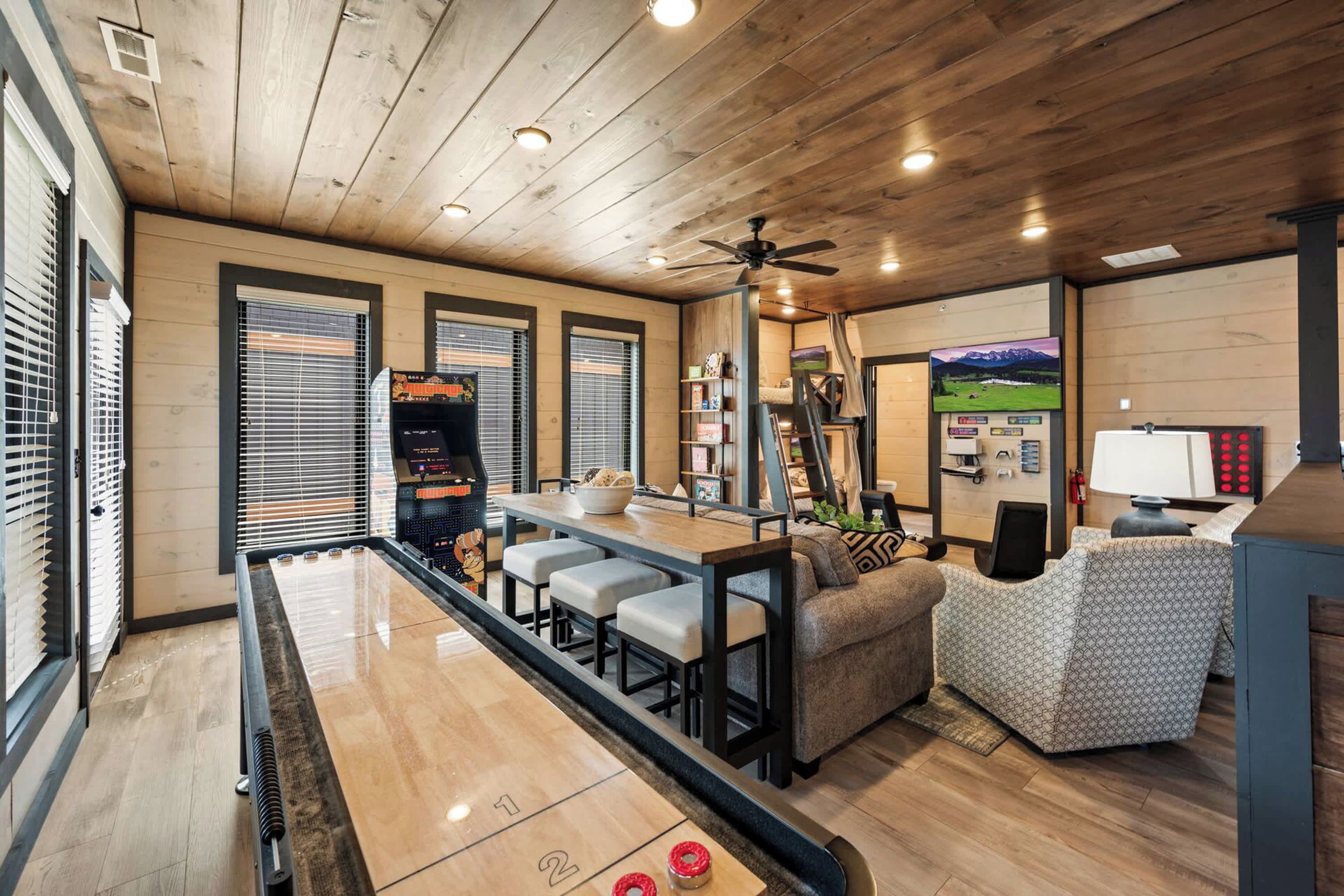 A room with a shuffleboard table, bar area, seating, and a television.