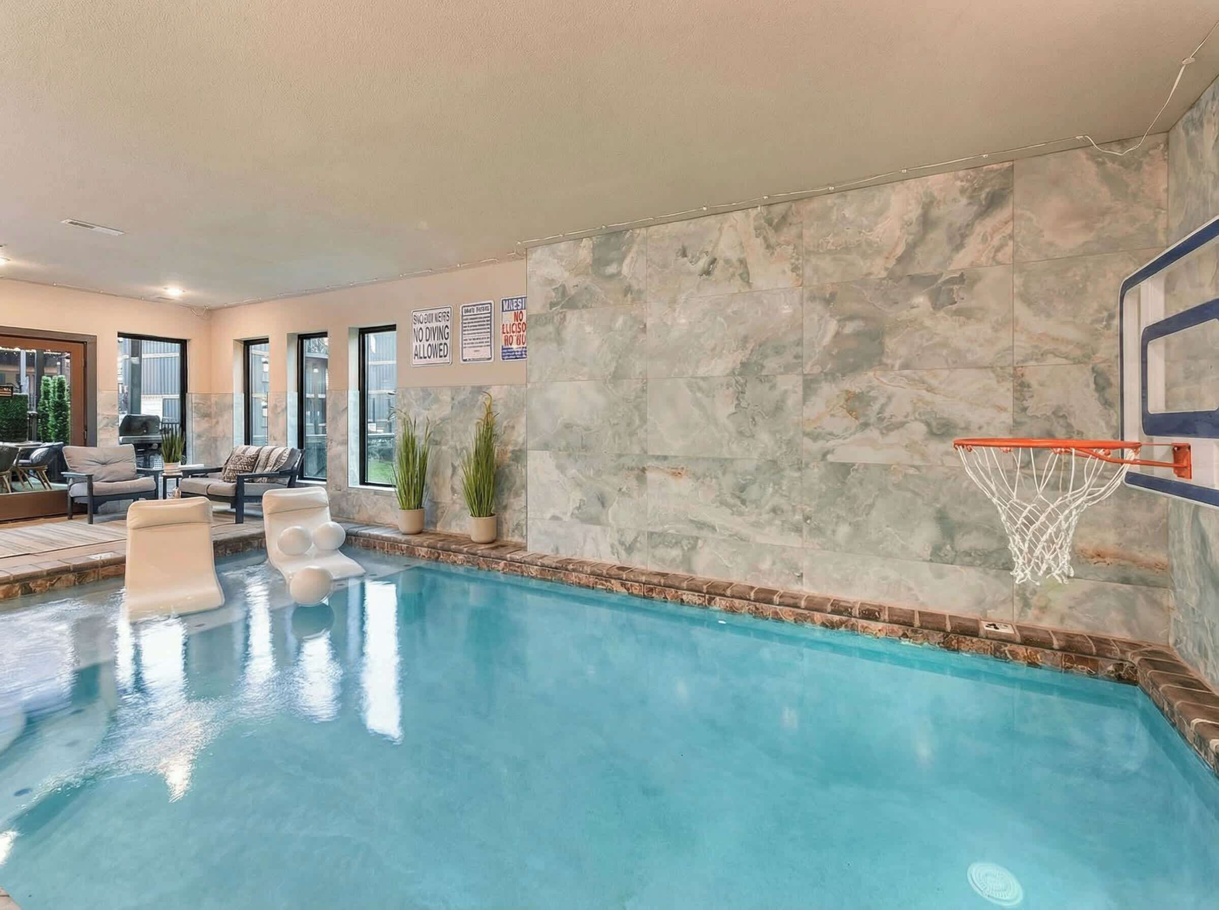 Une piscine intérieure équipée d’un panier de basketball, d’un espace détente et de plantes en pot.