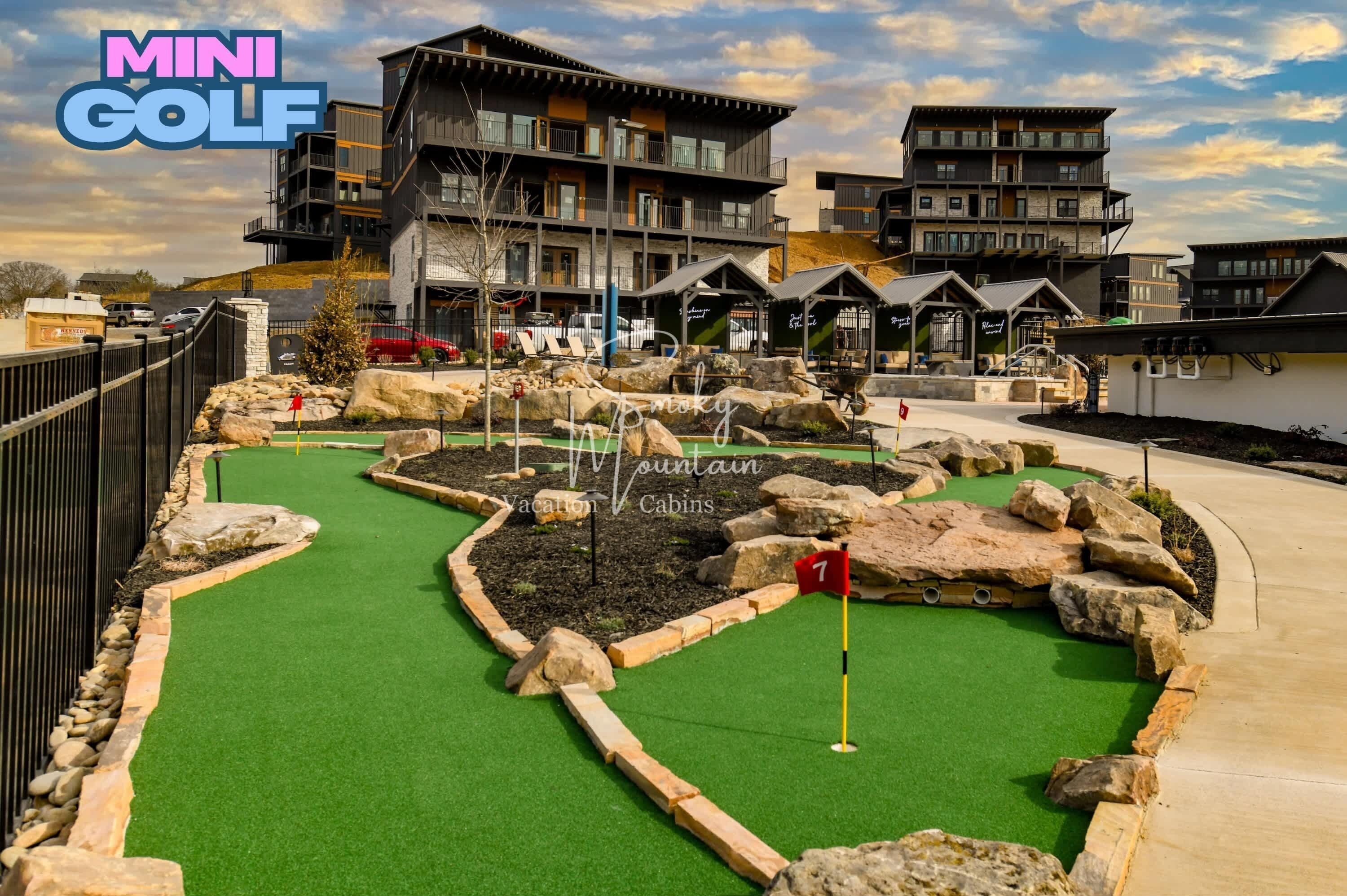 Ein Minigolfplatz mit grünem Kunstrasen, umgeben von Steinen und einem Holzaushügel.