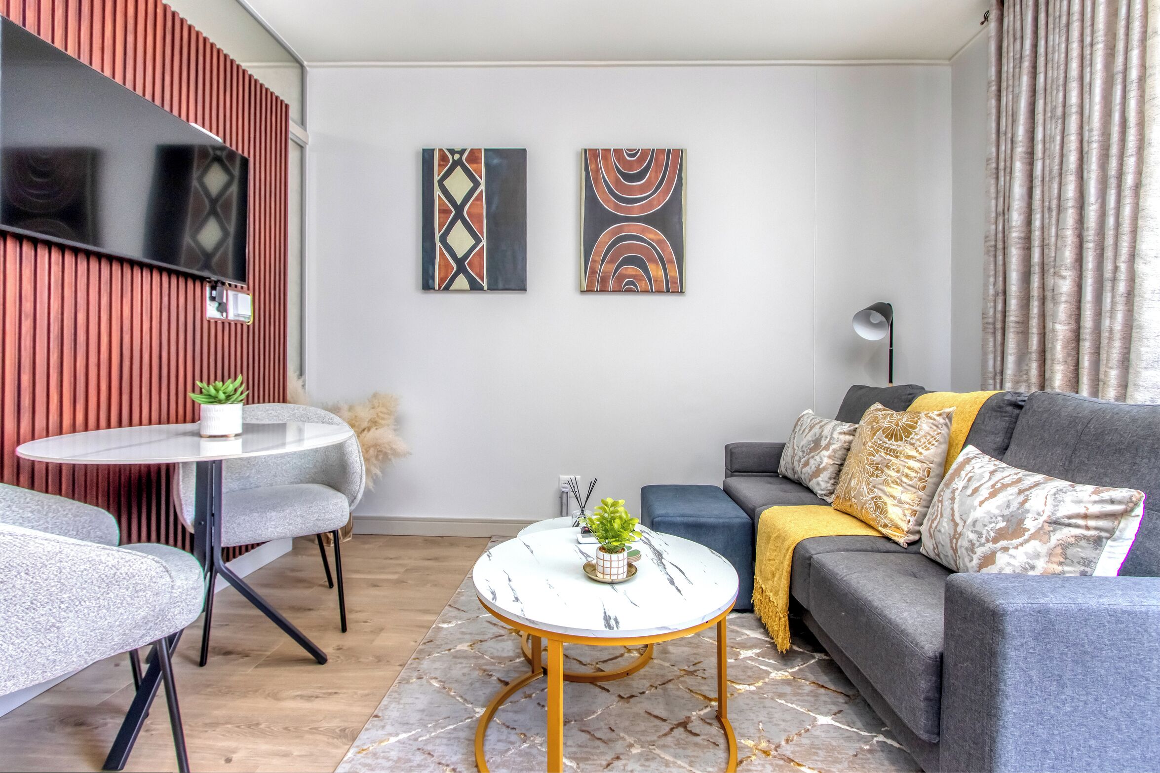 Ein modernes Wohnzimmer mit einem grauen Sofa, einem runden Couchtisch und einem an einer Holzwand montierten Fernseher.