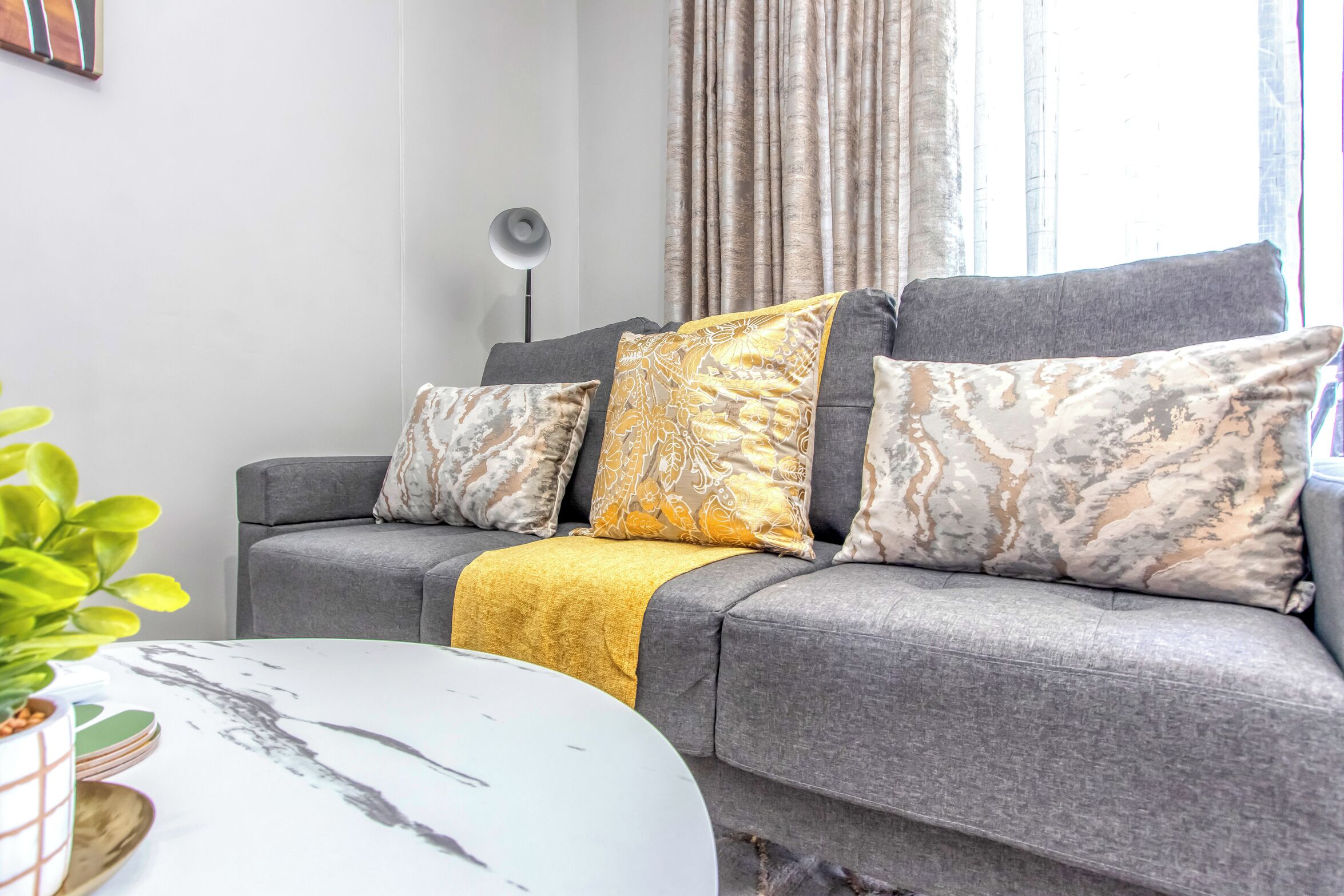 A grey sofa with patterned cushions, a yellow throw blanket, and a white coffee table with a marble design.