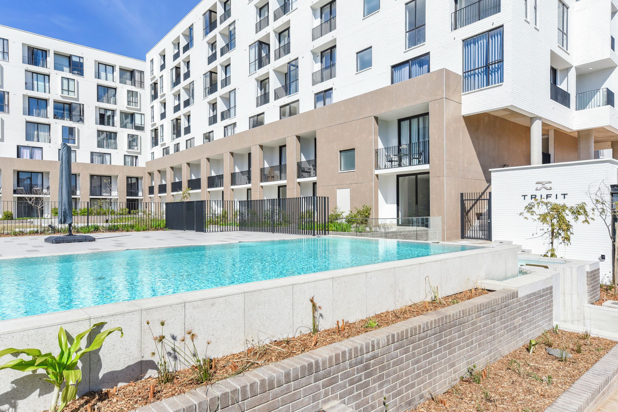 A modern building with a swimming pool, multiple balconies, and a gated entrance.
