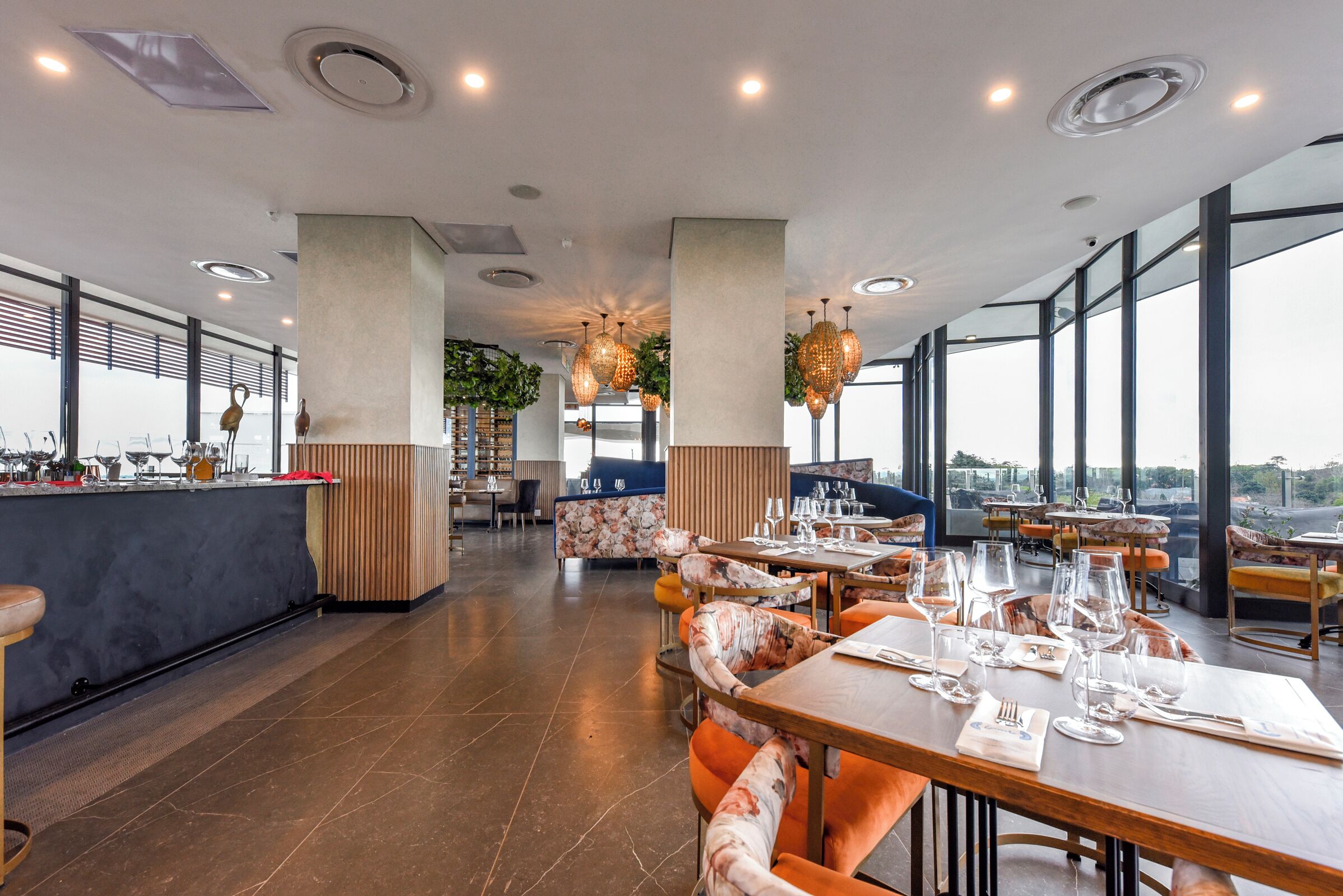 Un restaurant moderne doté de hauts plafonds, de grandes fenêtres et d’un agencement varié des espaces, comprenant des tables et des banquettes.