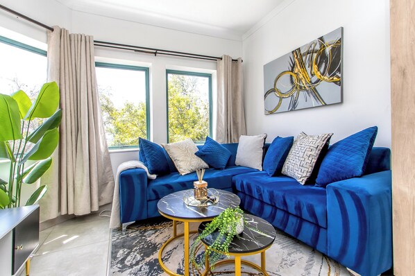 A modern living room with a blue sofa, a round coffee table, and a large window with curtains.