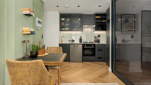 A modern kitchen with grey cabinets, a dishwasher, and an oven. There is a dining area with a table and chairs. - The Valour | Designer Apartment with Balcony (Cape Town)