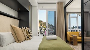 A hotel room with a bed, a sofa, a balcony with a view, and a sliding glass door. - The Valour | Designer Apartment with Balcony (Cape Town)