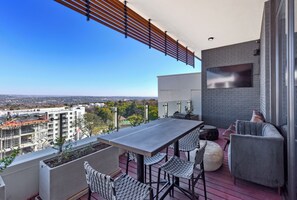 A balcony with a table and chairs, a TV mounted on the wall, and a view of the cityscape. - One Rosebank Suite | Effortless Style and Comfort (Johannesburg)