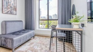 Una sala de estar moderna con un sofá gris, una mesa de comedor con una silla, un ventanal con cortinas y vistas a la ciudad.