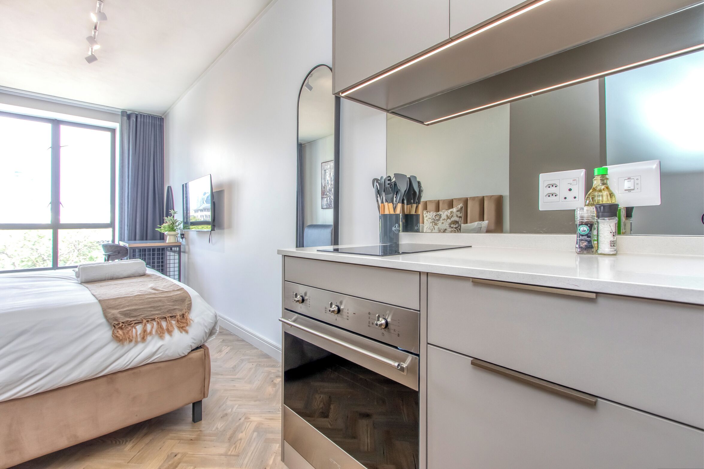Une chambre à coucher moderne avec un lit, un four encastré, un grand miroir et une fenêtre avec des rideaux.