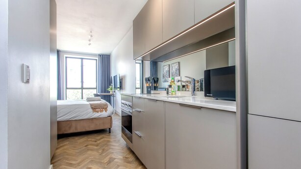 Una cocina compacta con electrodomésticos modernos, una zona de comedor con un banco, y un amplio ventanal que proporciona luz natural.