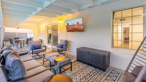 A covered outdoor seating area with a patterned floor, a sofa set, a table, and a wall-mounted TV. - Private Pool Paradise ~ 3BR Glendale Gem! (Glendale)