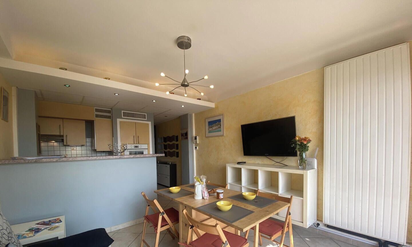 Zona pranzo con tavolo, sedie, televisione e cucina sullo sfondo.